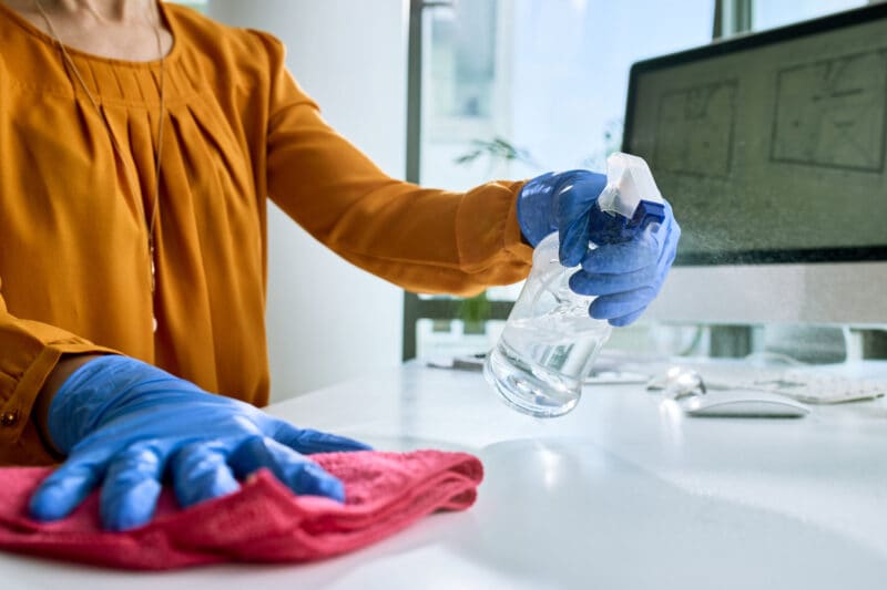 Close-up of businesswoman disinfecting her office desk.
