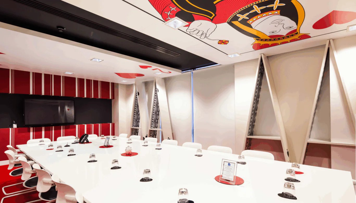The Queen of Hearts meeting room at OSiT Waterloo, featuring a bold red and white design with playing cards painted on the ceiling as part of the Alice in Wonderland theme.