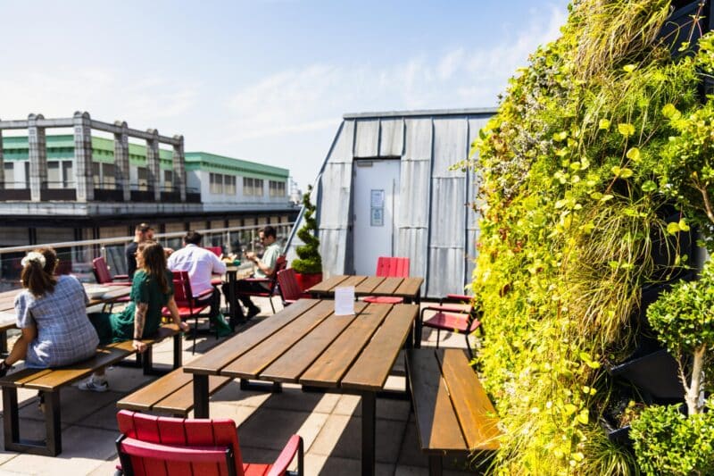 An outdoor breakout space at Office Space in Town Blackfriars, showcasing the colorful flower wall and relaxing terrace area designed for client networking and employee wellbeing.